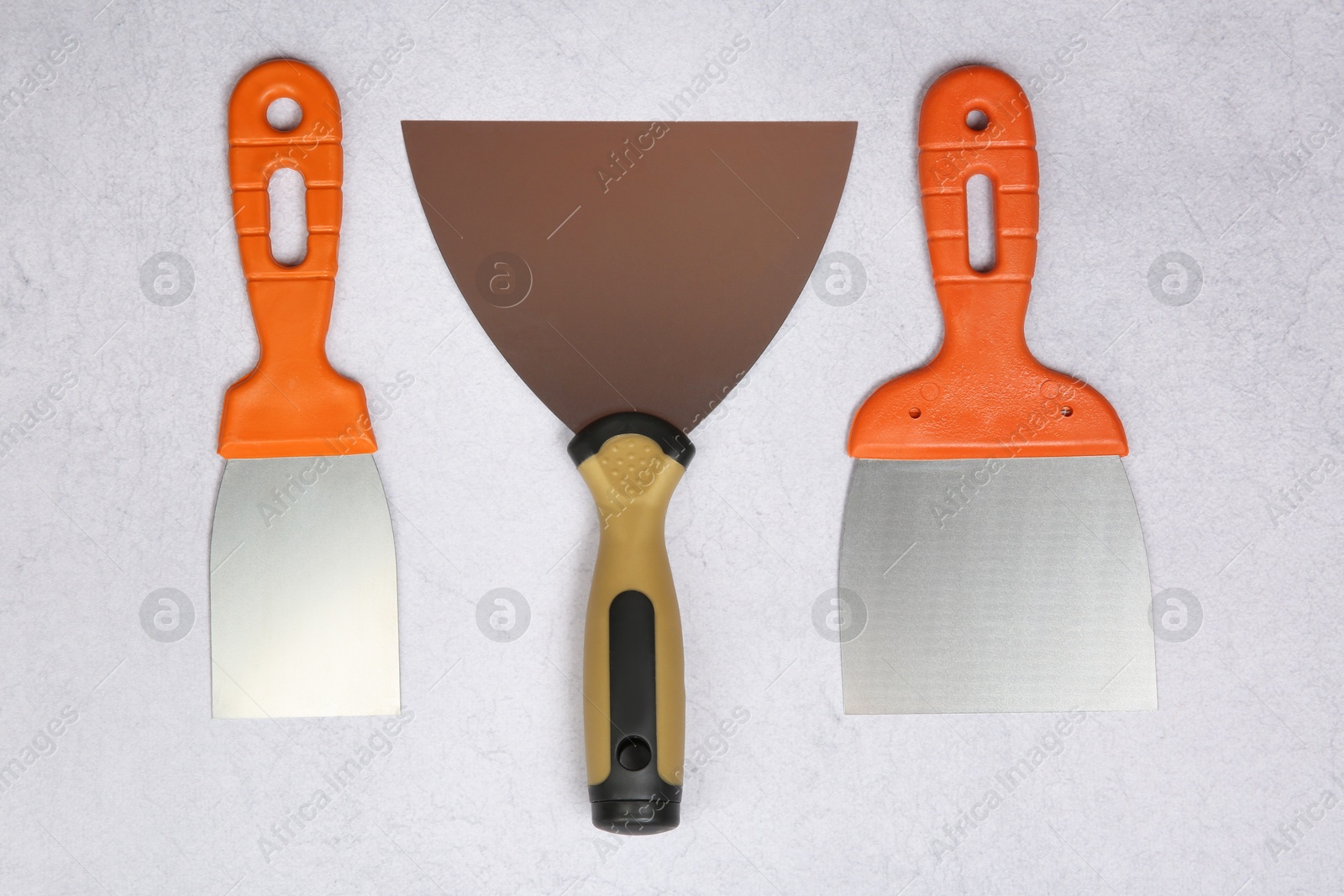 Photo of Different trowels on light textured table, flat lay. Construction tools