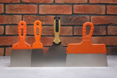 Photo of Different trowels on light textured table against red brick wall. Construction tools