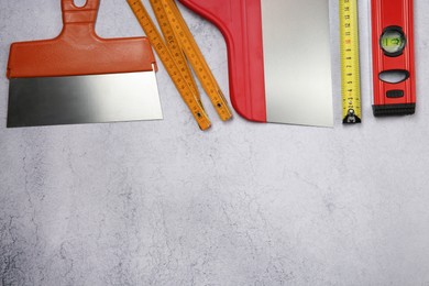 Trowels, building level and measuring tapes on grey textured table, flat lay. Space for text