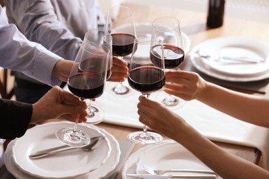 People clinking glasses of wine indoors, closeup