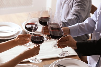 People clinking glasses of wine indoors, closeup