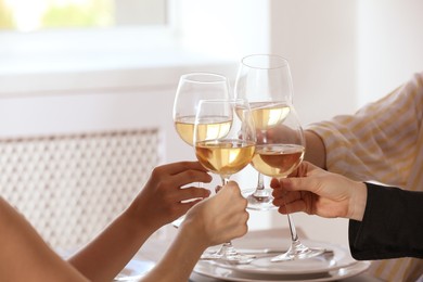 Photo of People clinking glasses of wine indoors, closeup