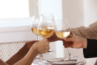 People clinking glasses of wine indoors, closeup