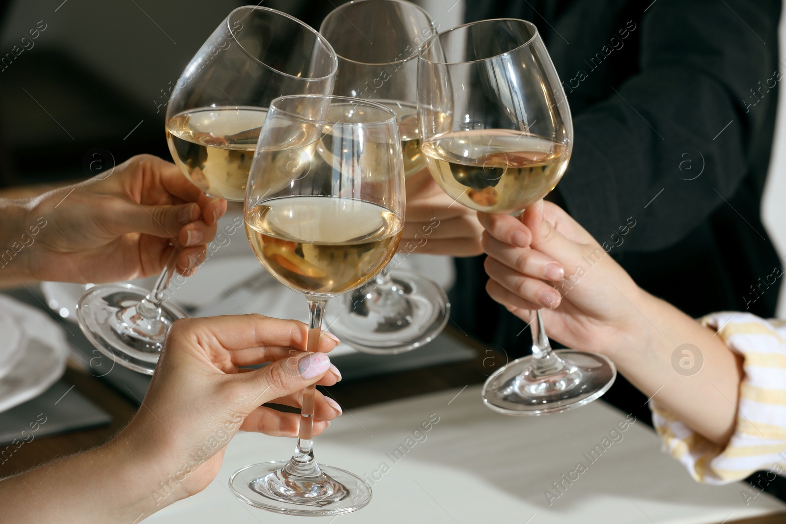 Photo of People clinking glasses of wine indoors, closeup