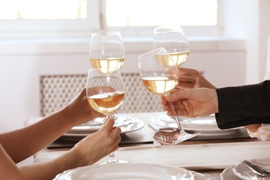 People clinking glasses of wine indoors, closeup