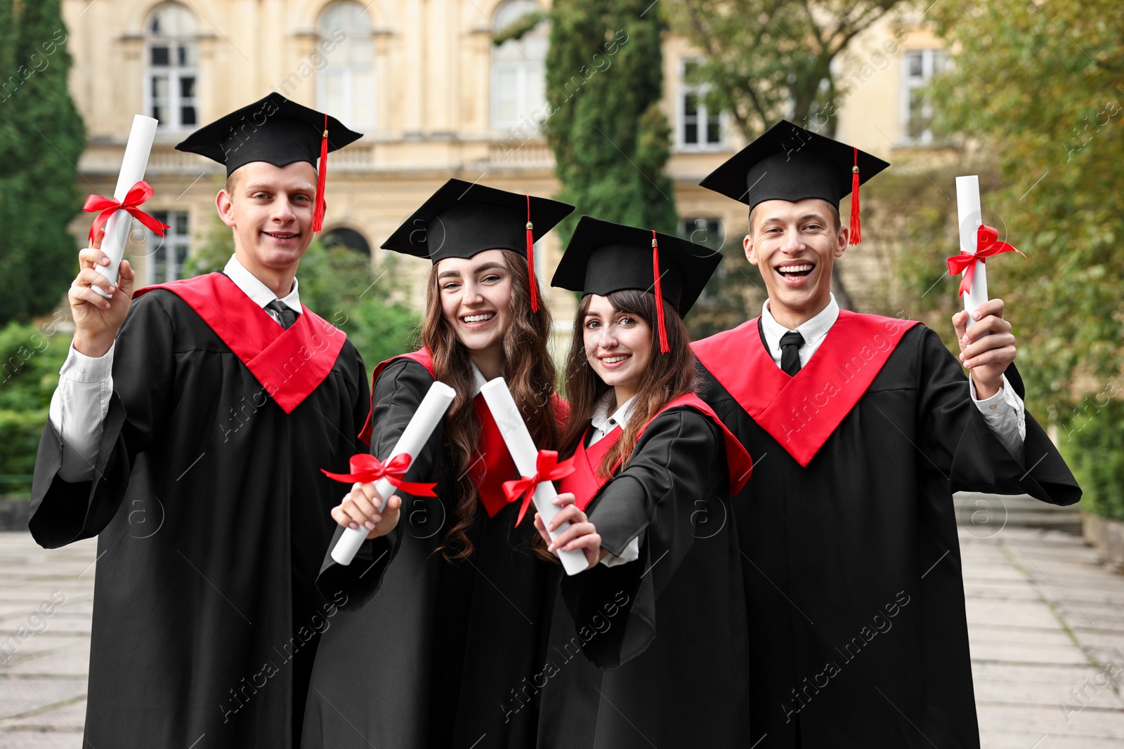 Photo of Happy students with diplomas after graduation ceremony outdoors