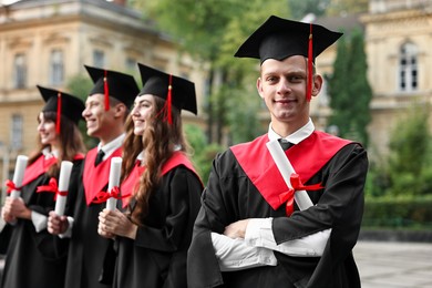 Happy students with diplomas after graduation ceremony outdoors, selective focus