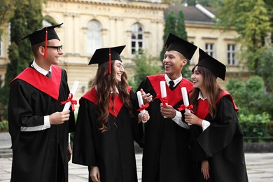 Photo of Happy students with diplomas after graduation ceremony outdoors