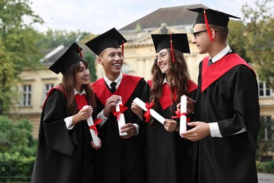 Happy students with diplomas after graduation ceremony outdoors