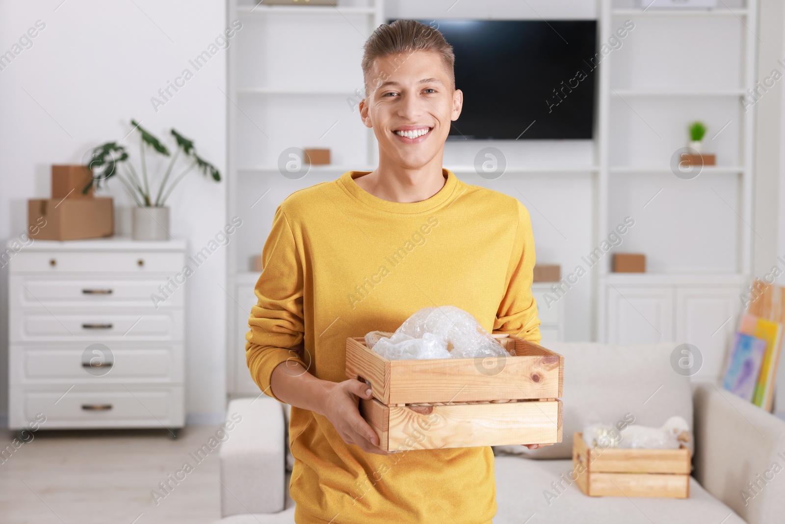 Photo of Happy man holding wooden crate with stuff in new apartment. Housewarming party