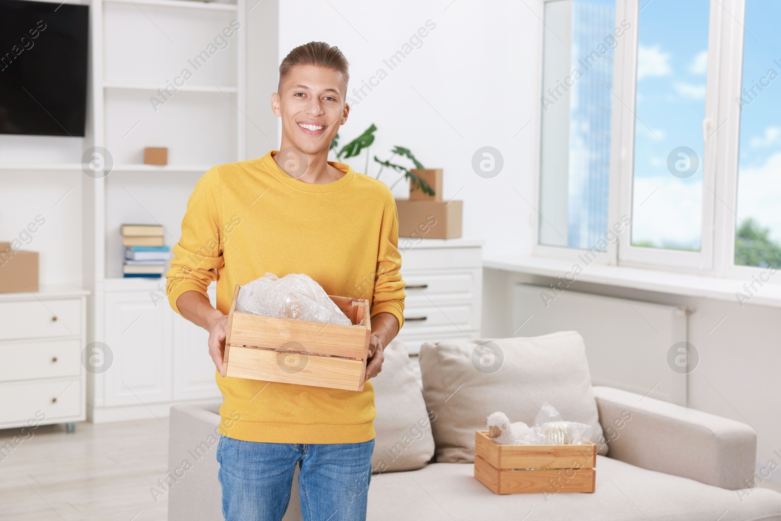 Photo of Happy man holding wooden crate with stuff in new apartment. Housewarming party