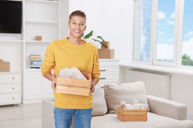 Happy man holding wooden crate with stuff in new apartment. Housewarming party