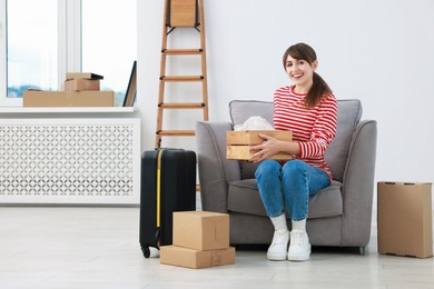 Photo of Happy woman with moving boxes and suitcase in new apartment. Housewarming party