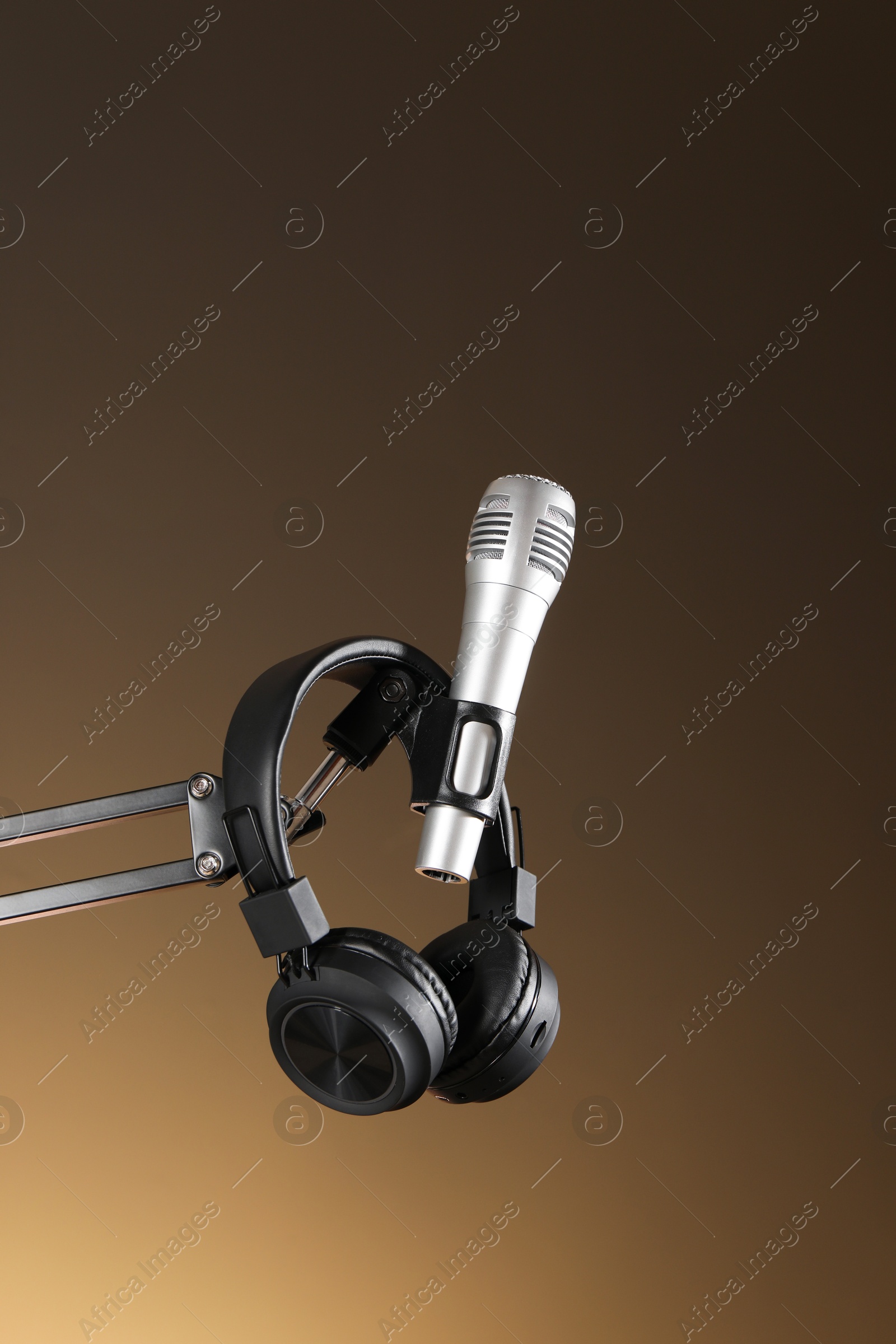 Photo of Stand with microphone and headphones on light brown background. Sound recording and reinforcement