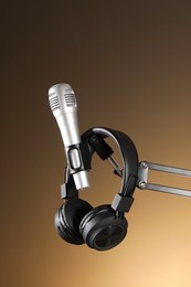 Photo of Stand with microphone and headphones on light brown background. Sound recording and reinforcement