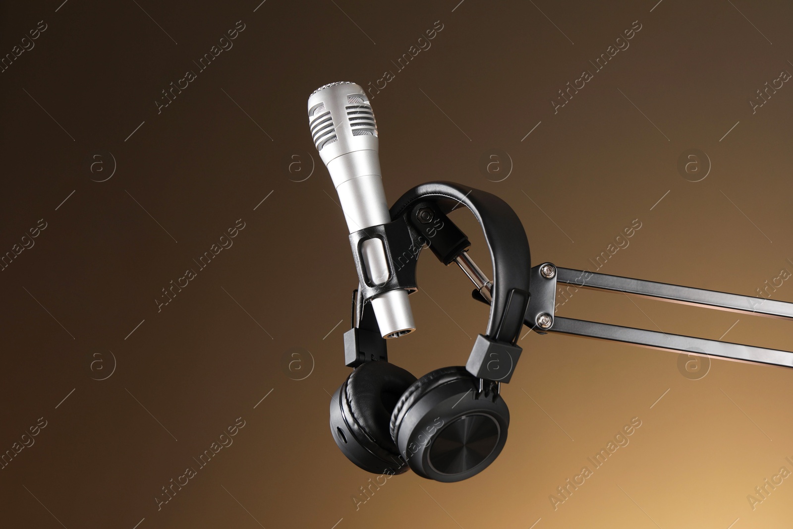 Photo of Stand with microphone and headphones on light brown background, low angle view. Sound recording and reinforcement