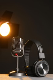 Photo of Vintage microphone and headphones on table against black background. Sound recording and reinforcement