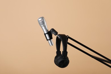 Photo of Stand with microphone and headphones on beige background. Sound recording and reinforcement