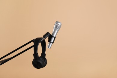 Photo of Stand with microphone and headphones on beige background, space for text. Sound recording and reinforcement