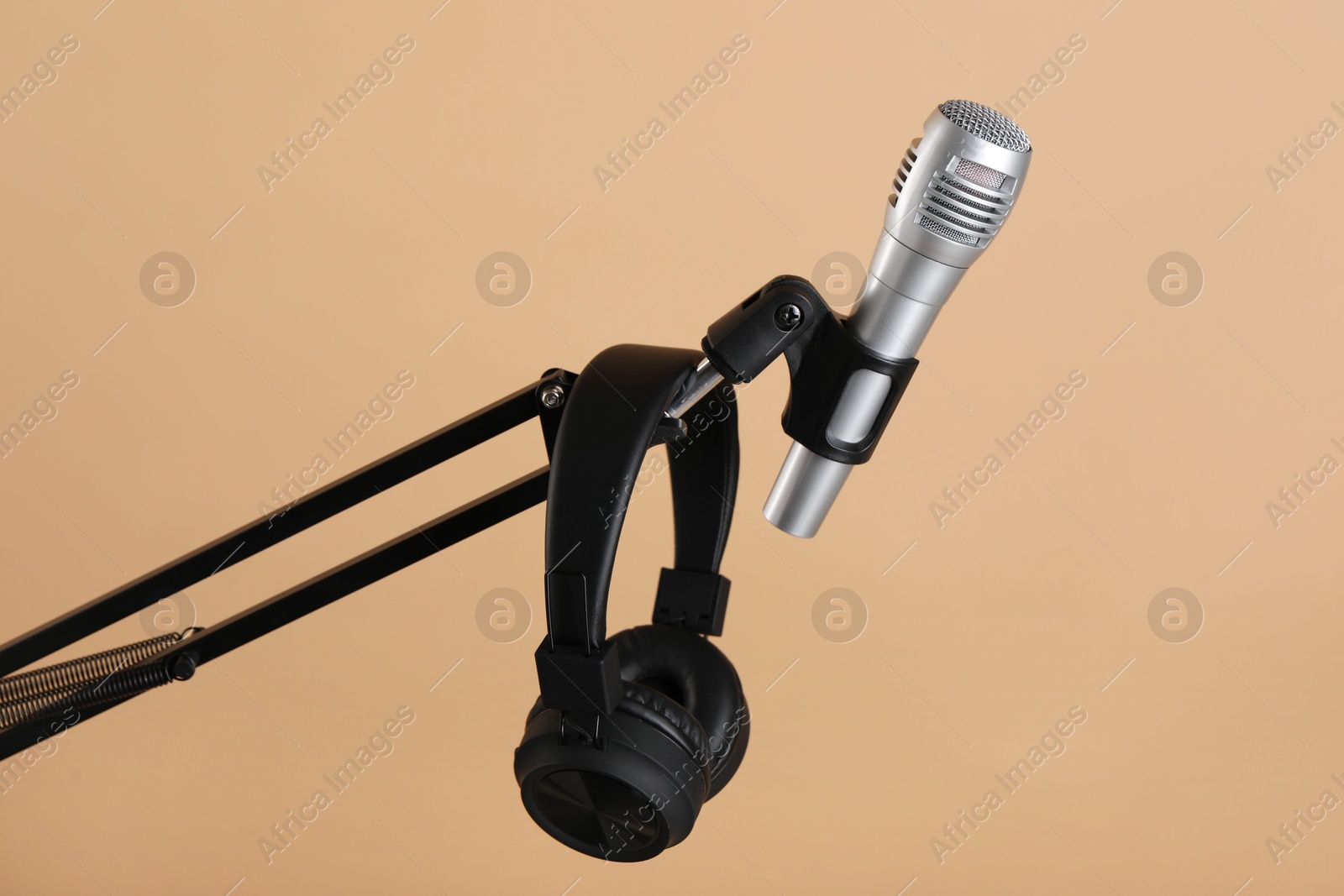 Photo of Stand with microphone and headphones on beige background. Sound recording and reinforcement