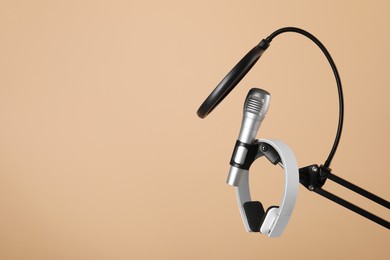 Photo of Stand with microphone, headphones and pop filter on beige background, space for text. Sound recording and reinforcement