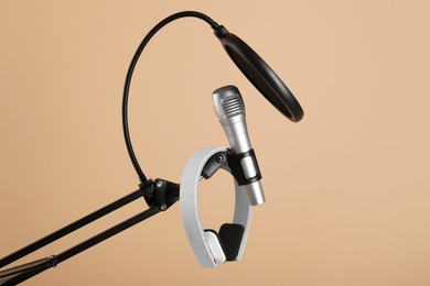 Photo of Stand with microphone, headphones and pop filter on beige background. Sound recording and reinforcement