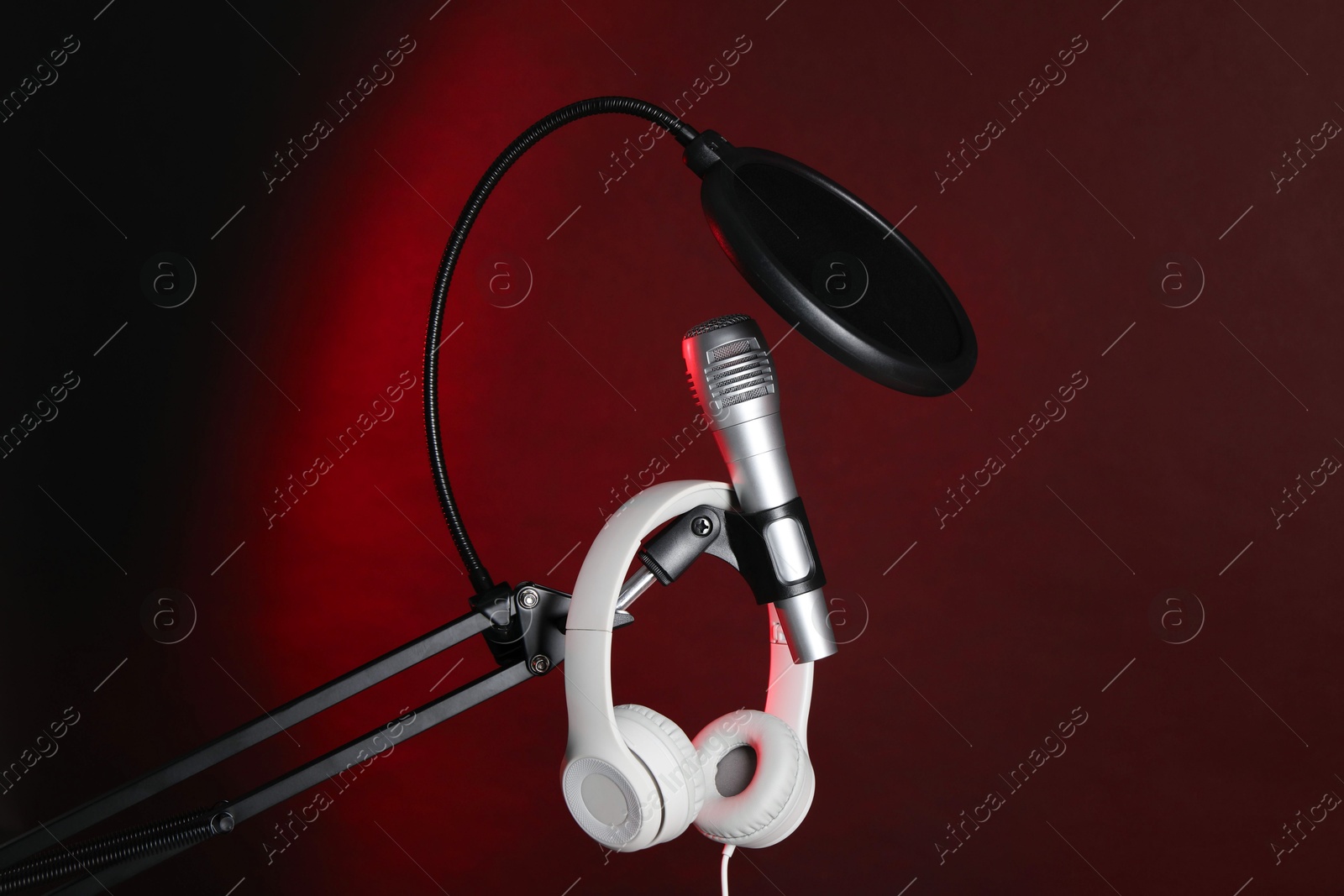 Photo of Stand with microphone, headphones and pop filter on dark background. Sound recording and reinforcement