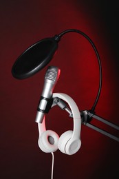 Photo of Stand with microphone, headphones and pop filter on dark background. Sound recording and reinforcement