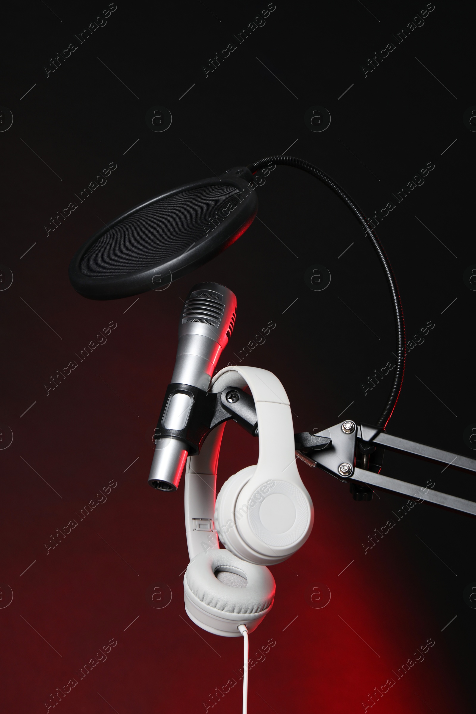 Photo of Stand with microphone, headphones and pop filter on dark background. Sound recording and reinforcement