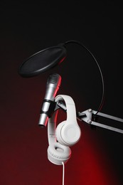 Photo of Stand with microphone, headphones and pop filter on dark background. Sound recording and reinforcement