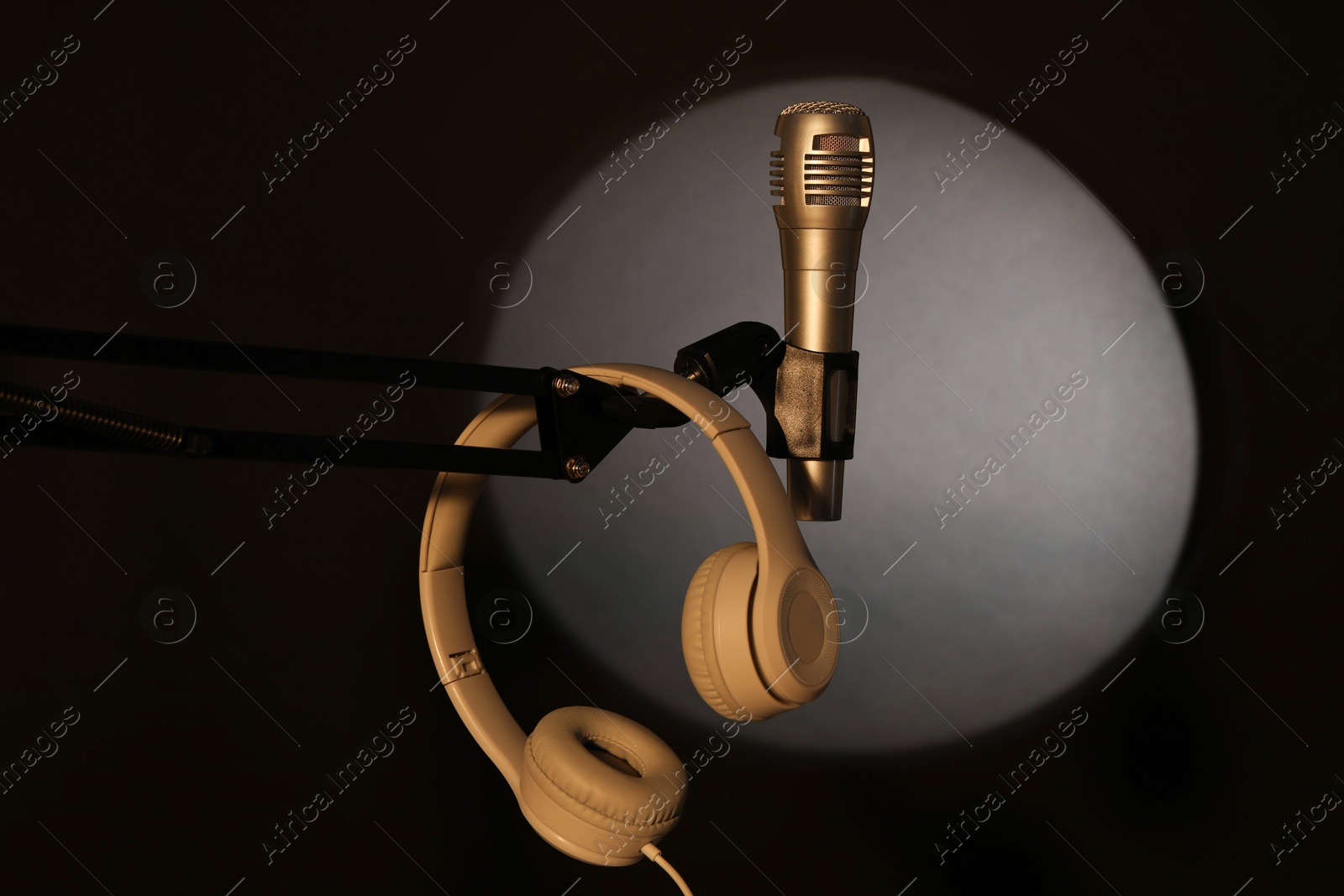 Photo of Stand with microphone and headphones in spotlight on black background. Sound recording and reinforcement