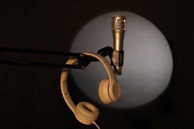 Photo of Stand with microphone and headphones in spotlight on black background. Sound recording and reinforcement