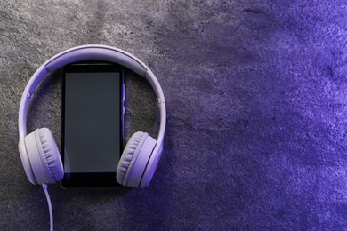 Photo of Smartphone with blank screen and headphones on grey textured background, top view with space for text. Sound equipment