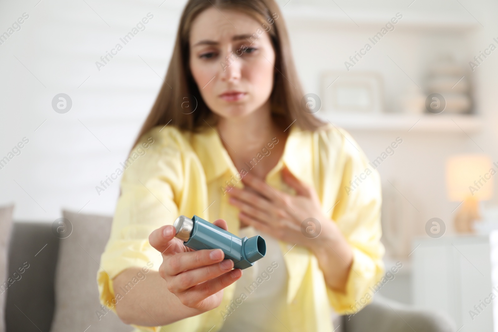 Photo of Young woman with asthma inhaler at home, selective focus