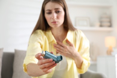 Photo of Young woman with asthma inhaler at home, selective focus