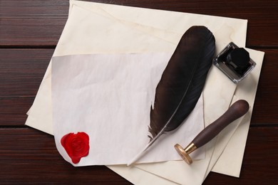 Photo of Old letter, wax stamps, feather, inkwell and envelopes on wooden table, top view