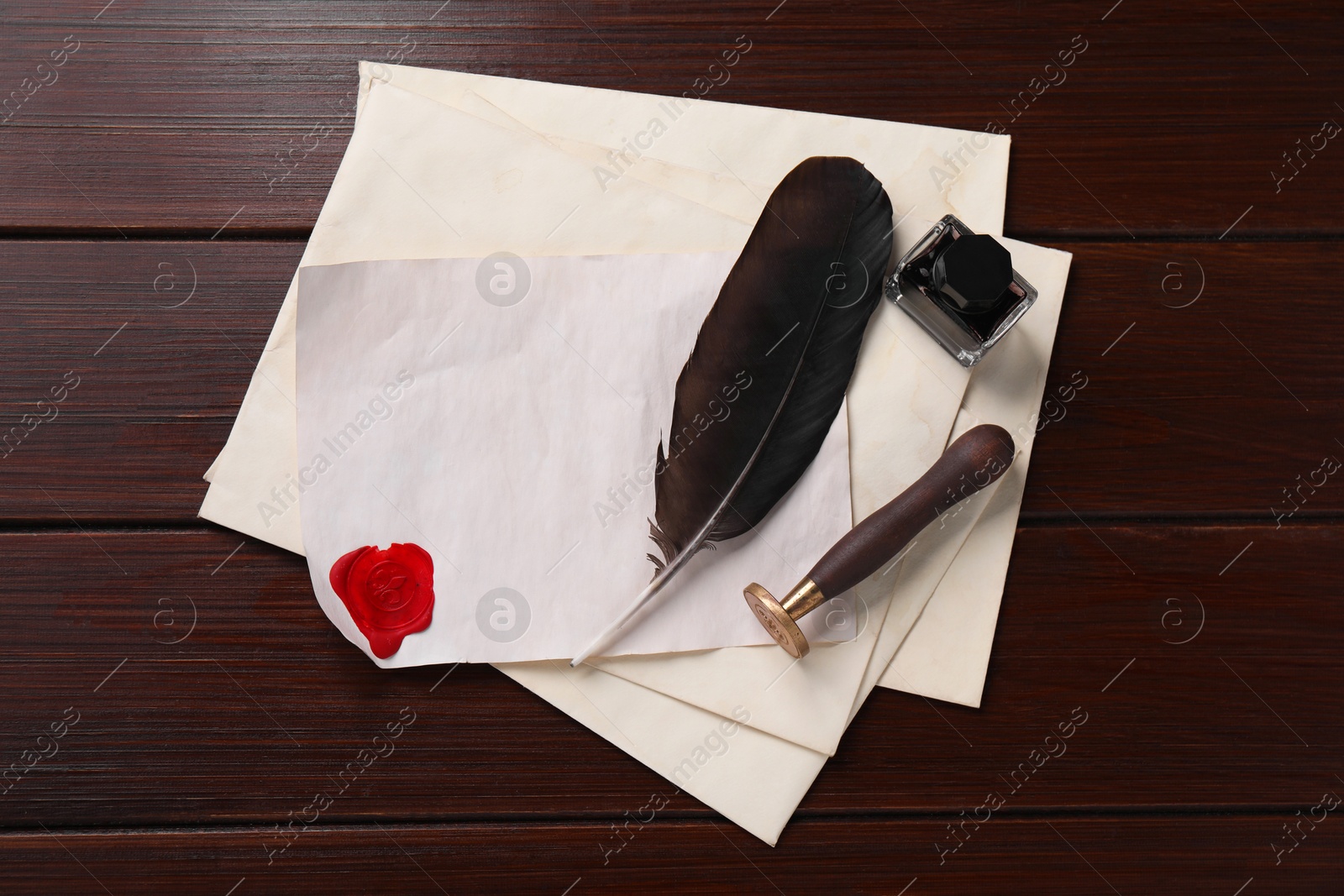 Photo of Old letter, wax stamps, feather, inkwell and envelopes on wooden table, top view