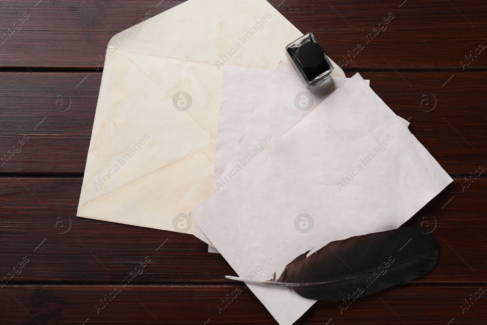 Photo of Old letters, envelope, feather and inkwell on wooden table, top view