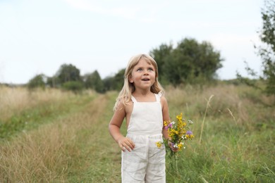 Cute little girl with flowers at meadow. Child enjoying beautiful nature