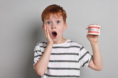 Photo of Dental phobia. Scared boy with model of jaw on grey background