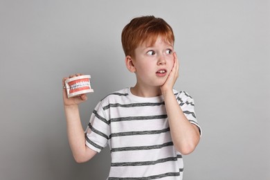 Photo of Dental phobia. Scared boy with model of jaw on grey background