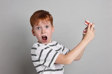 Dental phobia. Scared boy with model of jaw on grey background