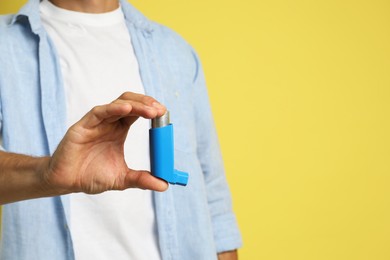 Man holding asthma inhaler on yellow background, closeup. Space for text