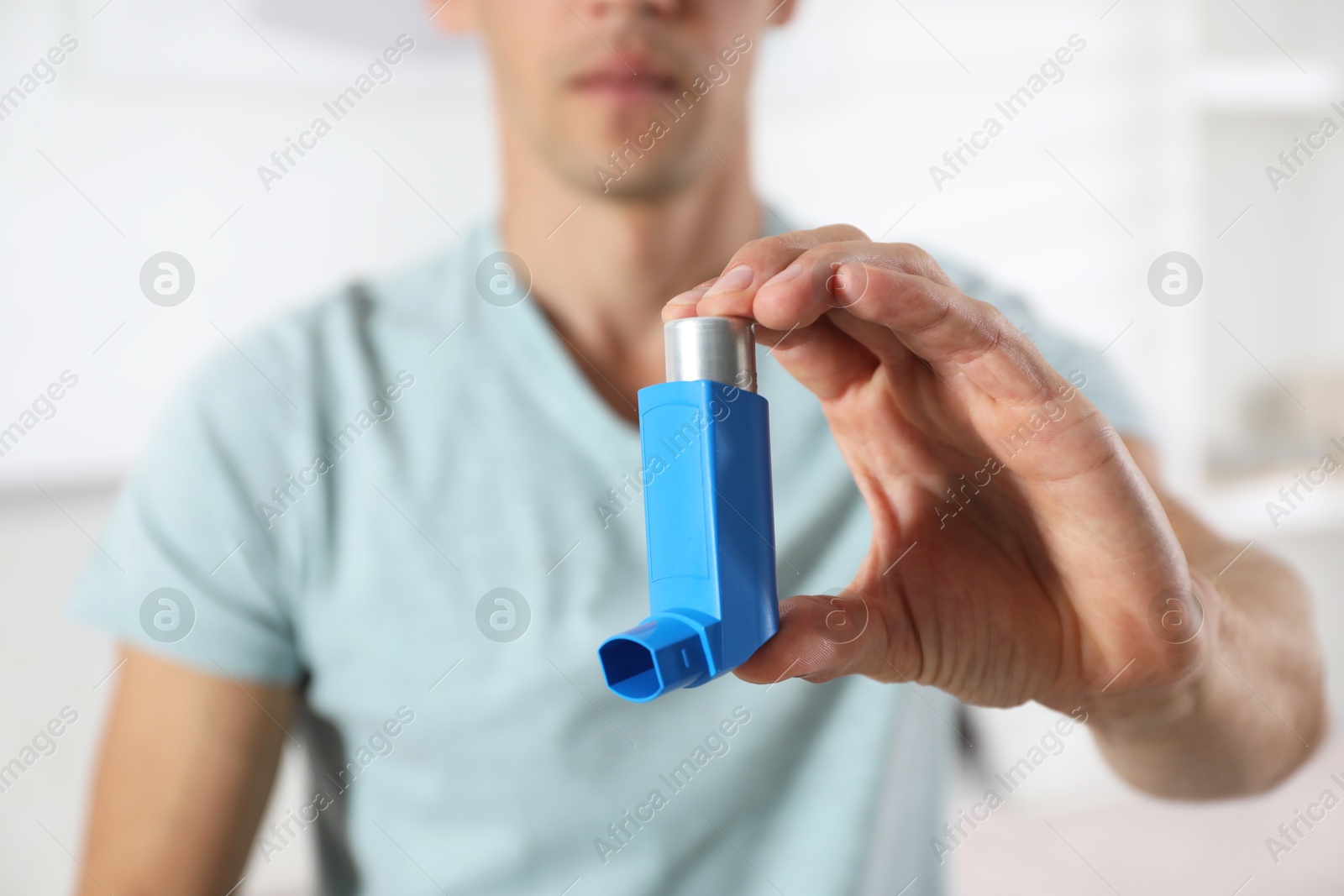 Photo of Man holding inhaler indoors, closeup. Asthma treatment