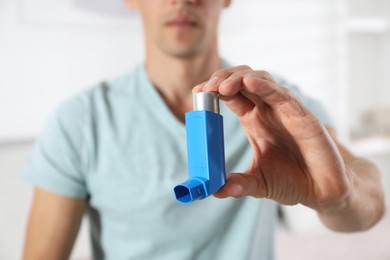 Man holding inhaler indoors, closeup. Asthma treatment