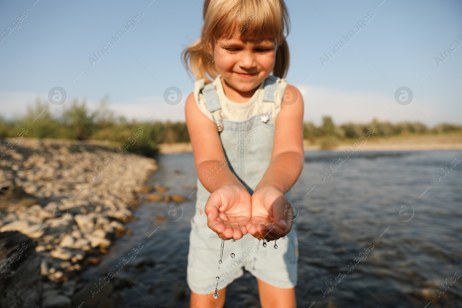 Photo of Cute little girl playing with water near river. Child enjoying beautiful nature