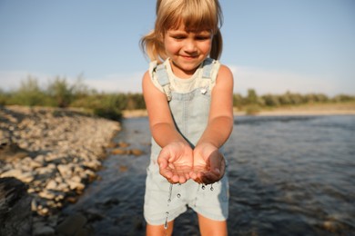 Cute little girl playing with water near river. Child enjoying beautiful nature