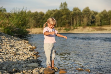 Photo of Cute little girl spending time near river. Child enjoying beautiful nature