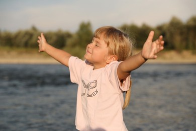 Photo of Cute little girl spending time near river. Child enjoying beautiful nature