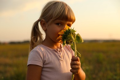 Photo of Cute little girl with sunflower at meadow. Child enjoying beautiful nature